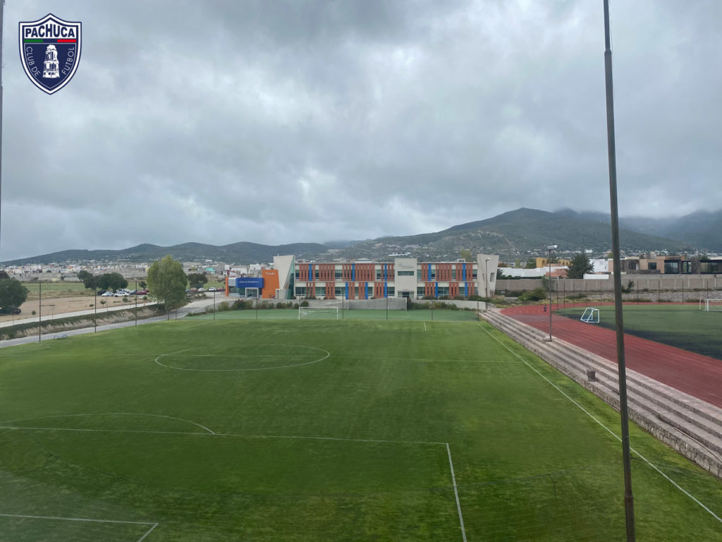 Cancha de pasto natural equipada con banquillos para dos equipos para uso de la Universidad del Futbol, fuerzas básicas, otros equipos del club y otros usuarios.