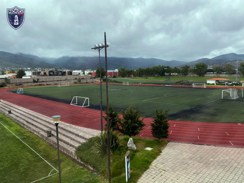 Cancha de pasto sintético equipada con iluminación, pista de tartán, banquillos para dos equipos para uso de la Universidad del Futbol, fuerzas básicas, otros equipos del club y otros usuarios.
