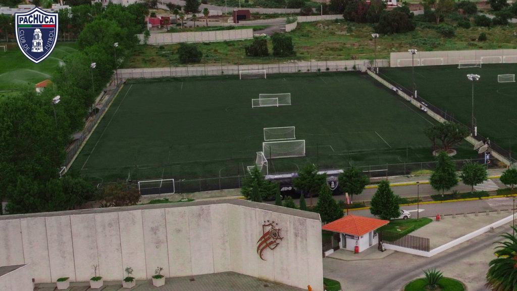 Cancha de pasto sintético equipada con iluminación, banquillos para dos equipos para uso de la Universidad del Futbol, otros equipos del club y otros usuarios.