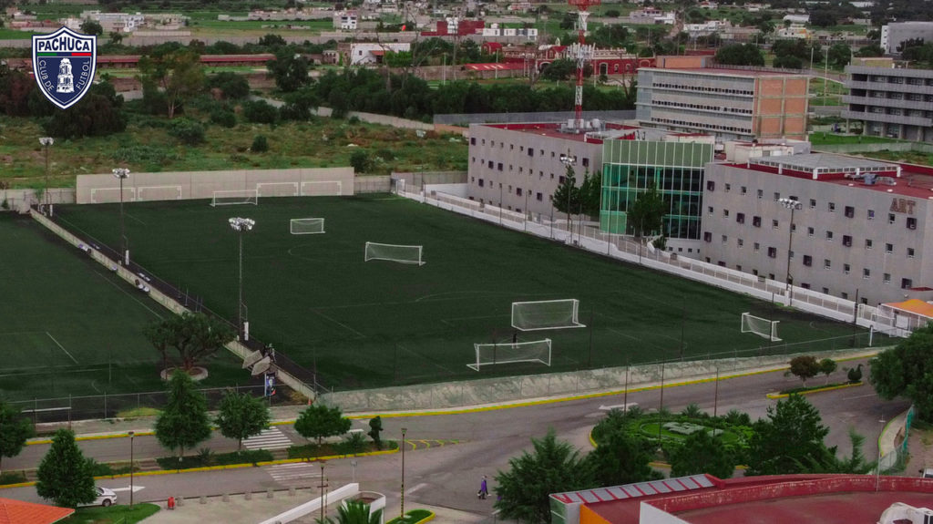 Cancha de pasto sintético equipada con iluminación, banquillos para dos equipos y pared de rebote para uso de la Universidad del Futbol, otros equipos del club y otros usuarios.